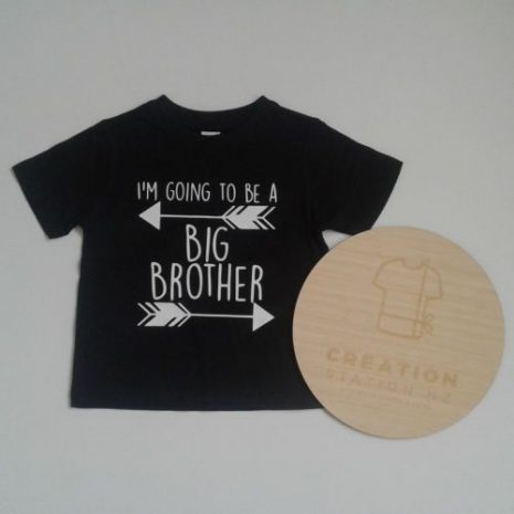 A black tee sits on a white background. It has a white print that reads "I'm Going to be a" above an arrow then "BIG BROTHER" centred with another arrow underneath going the opposite way.